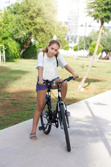 Naklejka premium Fashionable young teen girl in shorts and t-shirt rides a bicycle in a summer park