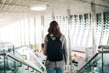 Girl in casual clothes standing at the airport with backpack and coffee cup. Travel and vacation vibes.