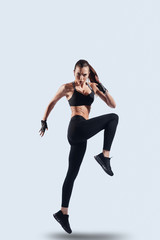 Fototapeta na wymiar Keep moving! Full length of attractive young woman in sports clothing looking at camera while hovering against grey background