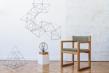 Minimalistic and modern interior of open space with design green armchair, triangle geometric sculpture , stylish lamp and elegant accessories. Abstract paintings on the white wall. Template.