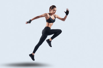Fototapeta na wymiar Challenging herself. Full length of attractive young woman in sports clothing jumping while hovering against grey background