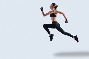 Fototapeta na wymiar Achieving best results. Full length of attractive young woman in sports clothing exercising while hovering against grey background