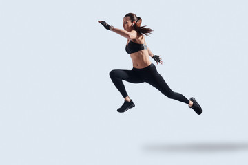 Fototapeta na wymiar Motivated to shape her body. Full length of attractive young woman in sports clothing exercising while hovering against grey background