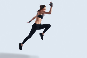 Fototapeta na wymiar Real freedom. Full length of attractive young woman in sports clothing exercising while hovering against grey background