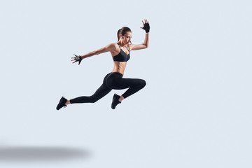 Every day filled with sport. Full length of attractive young woman in sports clothing exercising while hovering against grey background