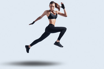 Fototapeta na wymiar Act now! Full length of attractive young woman in sports clothing looking at camera while hovering against grey background