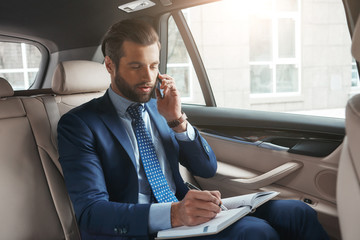 Important talk with client. Busy young businessman in formal wear writing something in his notebook...