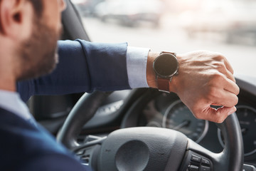 What time is it? Cropped image of bearded businessman is looking at watch on his hand while sitting...