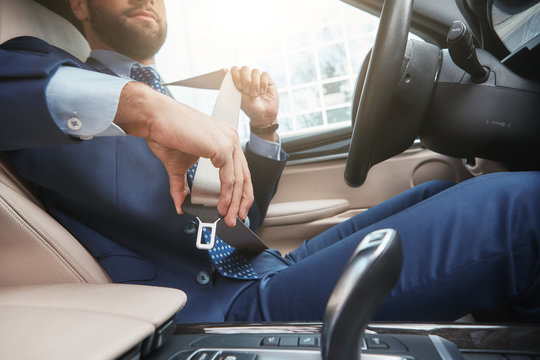Safe driving. Cropped image of young businessman in formal wear is fastening the seat belt while sitting in his car