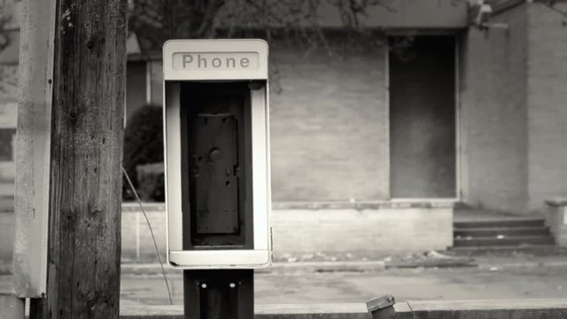 An abandoned outdated phone booth, in a neglected neighborhood of a big American city. Sepia toning. Handheld shot.