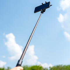 Smartphone on a selfie stick in male hand against the sky.