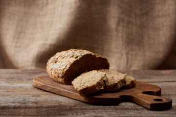 delicious sliced brown bread on wooden chopping board with sackcloth on background