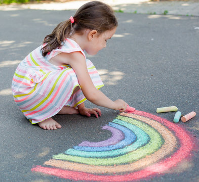 the child girl draws a rainbow with colored chalk on the asphalt. Child drawings paintings concept. Education and arts, be creative when back to school 