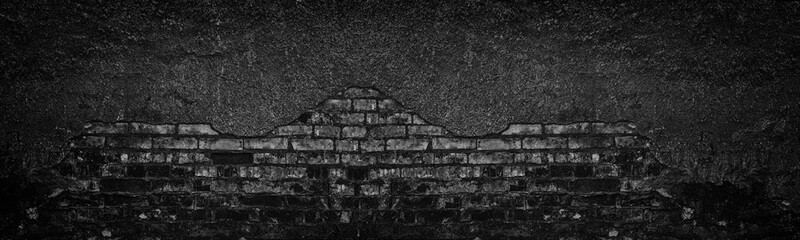 Black burnt brick wall with fallen off plaster wide texture. Crumbled old shabby brickwork. Dark gloomy large background