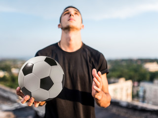 Fototapeta premium Man playing with ball outdoors on the roof on the background of the city