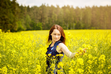 Naklejka na ściany i meble young woman in a field of rapeseed on a sunny day
