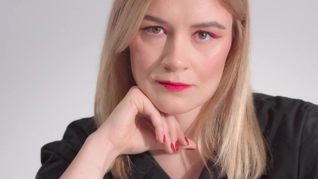 panned video portrait of blonde woman with bright red makeup waatching at camera werious