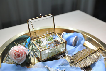 Beautiful wedding gold diamond rings are in a glass box on a gold tray decorated with flowers and decor. Close-up