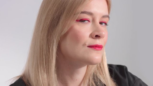 serious blonde woman turning to the camera and watching at camera stright. red eyewings makeup look