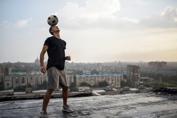 Man playing with ball outdoors on the roof on the background of the city