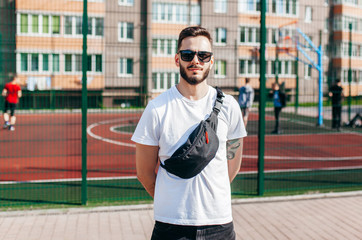 Obraz premium Stylish bearded hipster in the at the city in a white T-shirt with waist bag