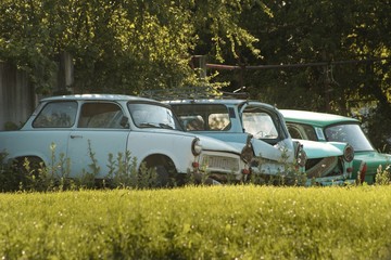 Four car wrecks stand in grass under trees.Four deserted cars in blue, green and beige color ,rot and rust in nature.