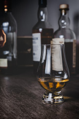Whisky glass with single malt scotch on wooden table and scotch bottles on the background