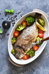 Baked dorado with spices, with broccoli and tomatoes on a concrete background.