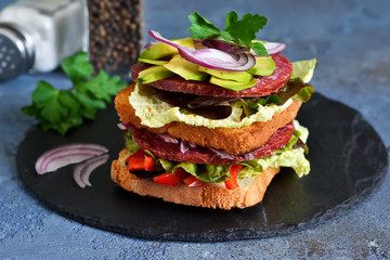 Crispy sandwich with salami, salad and vegetables on the kitchen table. View from above.