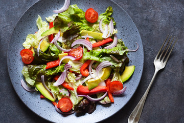Vegan salad cabbage, spinach, tomatoes, peppers, avocados, onions with olive oil on the kitchen table. View from above.