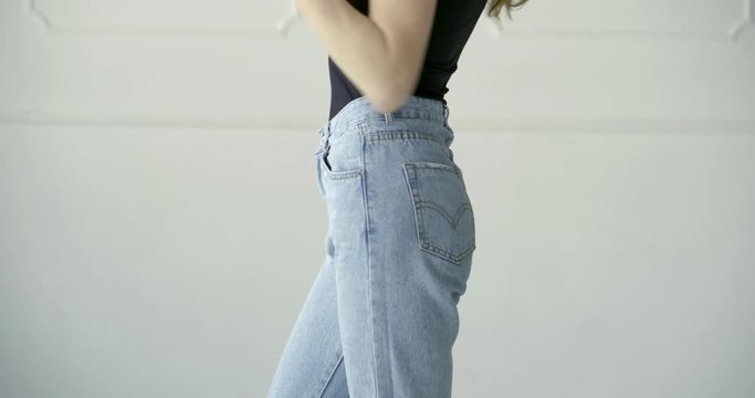 fashion model is demonstrating trendy denim pants, closeup of her slim hips in studio