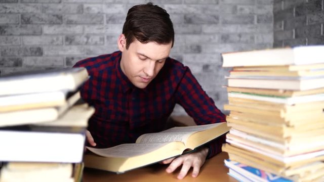 Man student boring reading book at library with a lot of books in university. Student disheartened reading book for examination.