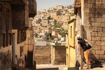 Young tourist girl looking behind the corner over the crowded neighbourhood in Turkish city of Sanliurfa. Old houses on the steep hill.