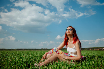 Girl sitting in a field on the green grass, blue sky background. Copy space