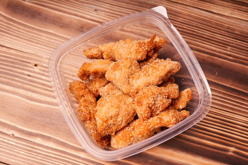 Chicken strips in a plastic container on a wooden table.