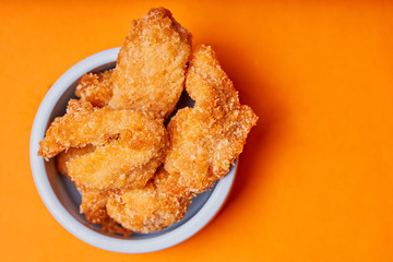 Chicken strips in a clay pot on an orange background.