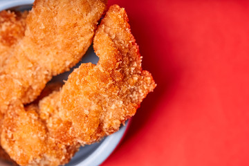 Chicken strips in a clay pot on an red background.