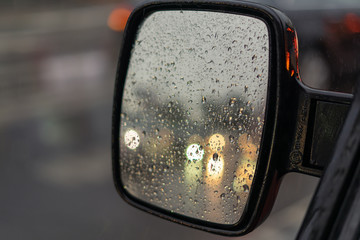 Raindrops on the rearview mirror of a car. In reflection, the headlights of other cars are out of focus.