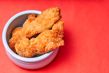 Chicken strips in a clay pot on an red background.