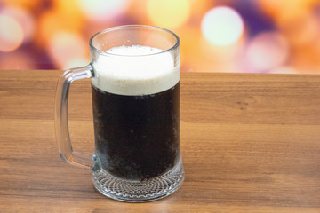 A glass of dark beer with white foam on a wooden table.