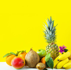 Composition from assortment of different tropical and summer seasonal fruits. Pineapple mango coconut citrus oranges lemons apples kiwi bananas on yellow background.Healthy diet vitamins vegan