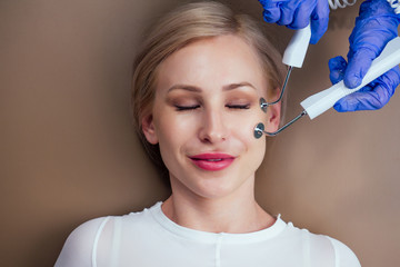 beauty aesthetic spa salon .blonde female getting instrument facial massaging with microcurrent electro instrument device.