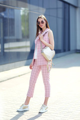 high fashion outdoor Portrait of a young woman. Pantsuit, pink color, long hair, sunglasses