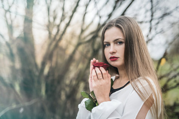 Beautiful young woman with red rose posing outdoors