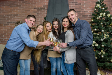 Friends in casual wear posing with champagne near fireplace