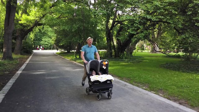 father with kids in double stroller in a park.  Man pushing twins stroller, pram.