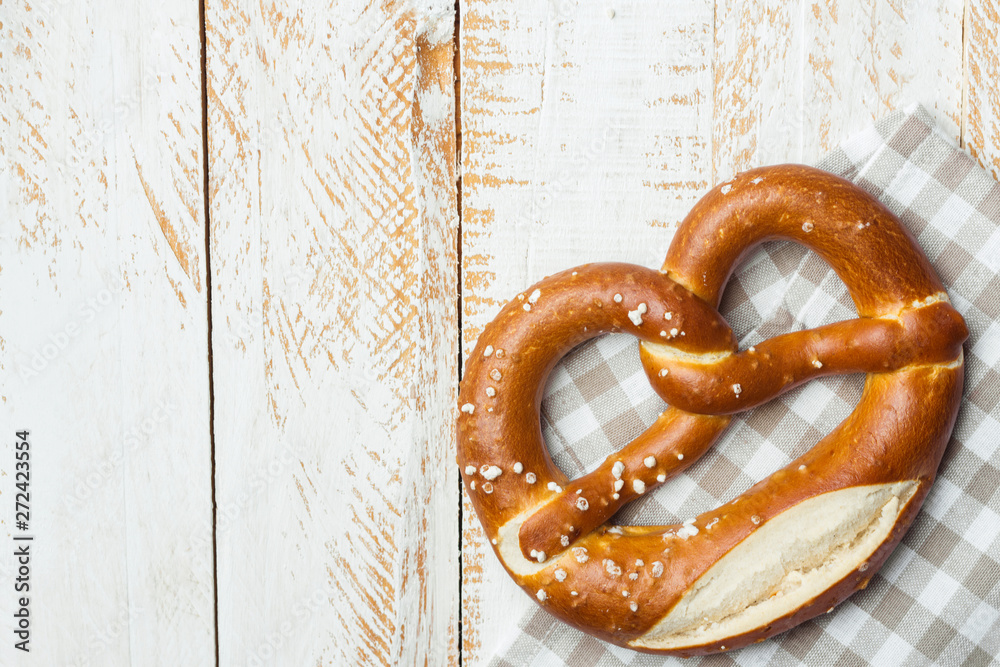 Wall mural Traditional German savory lye pretzel with salt on checkered cotton kitchen towel on white plank wood table. Poster banner for bakery coffee shop menu. Oktoberfest card. Copy space