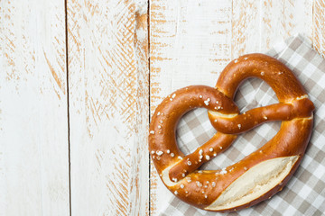Traditional German savory lye pretzel with salt on checkered cotton kitchen towel on white plank...