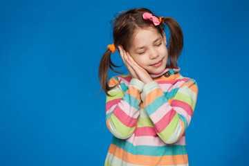 Portrait of an emotional girl of five years in a striped sweater on a blue background