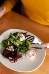 Woman is eating a healthy beetroot salad with greens, almond and cream cheese, served on a wooden rustic table